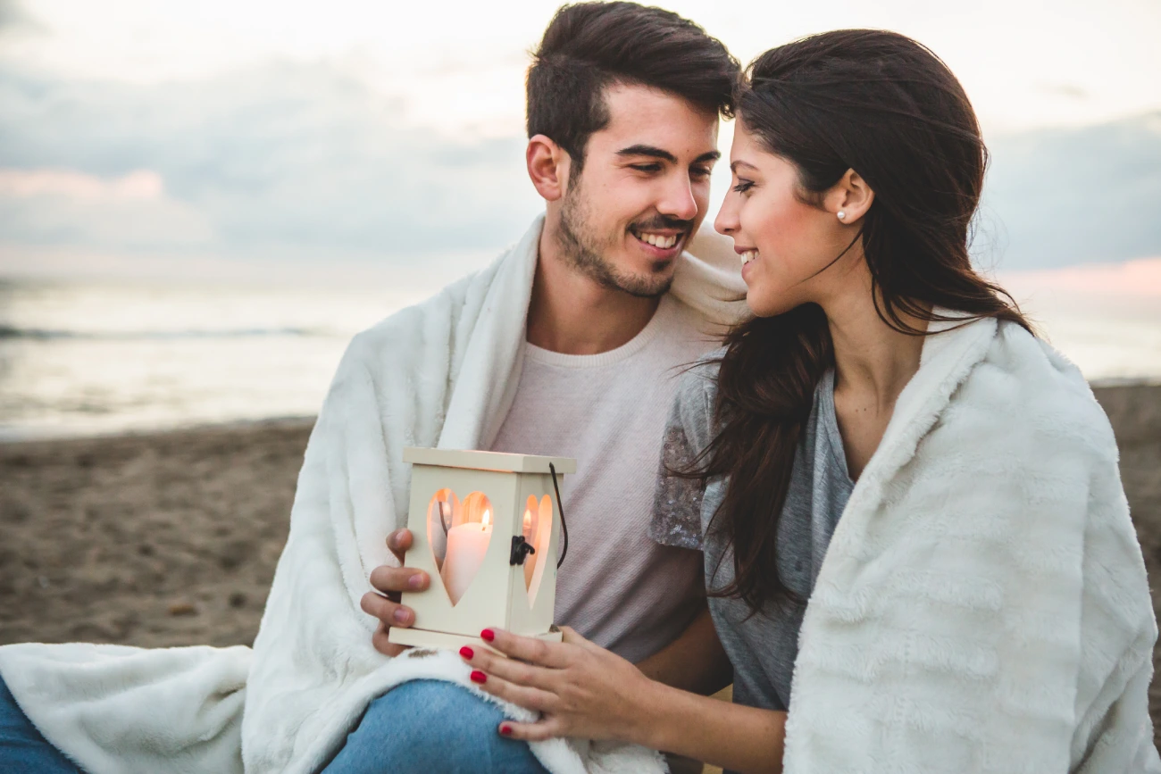 couple-sitting-sand-with-candle-blanket