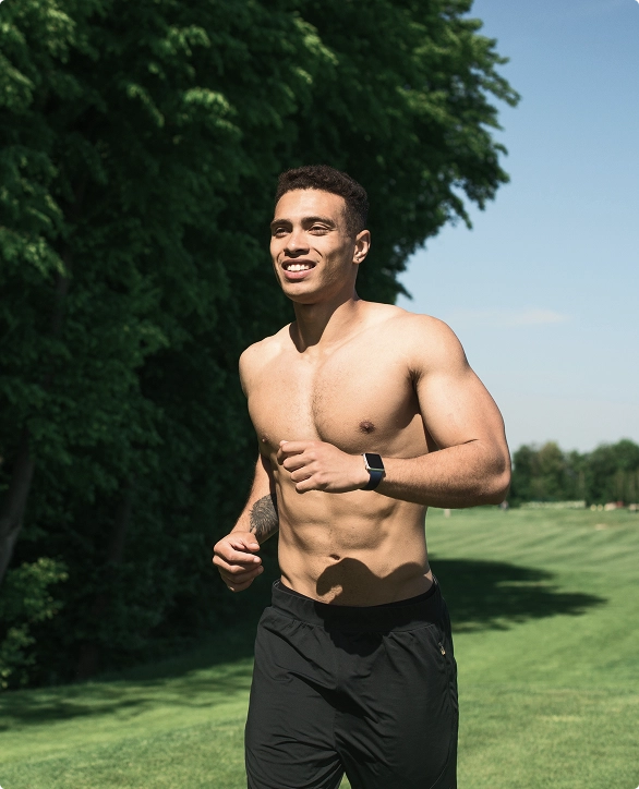 A shirtless man sprinting across a lush green field under a clear blue sky. A shirtless man sprinting across a lush green field under a clear blue sky.