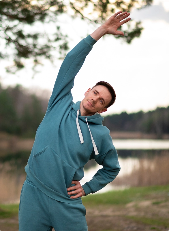 A man in a blue hoodie is stretching his arms overhead in a relaxed posture. A man in a blue hoodie is stretching his arms overhead in a relaxed posture.