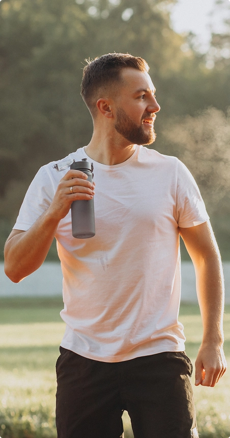 A man stands in a field, holding a water bottle, with green grass and a clear sky in the background. A man stands in a field, holding a water bottle, with green grass and a clear sky in the background.