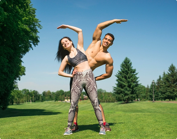 A man and woman practicing yoga poses together in a lush green field under a clear blue sky. A man and woman practicing yoga poses together in a lush green field under a clear blue sky.