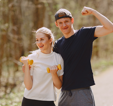 A man and woman exercising in the woods, each holding a dumbbell and focused on their workout. A man and woman exercising in the woods, each holding a dumbbell and focused on their workout.