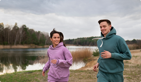 Two individuals jogging side by side along a scenic lake, surrounded by greenery and a clear blue sky. Two individuals jogging side by side along a scenic lake, surrounded by greenery and a clear blue sky.
