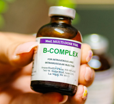 A hand holding a bottle of B complex vitamins against a neutral background.