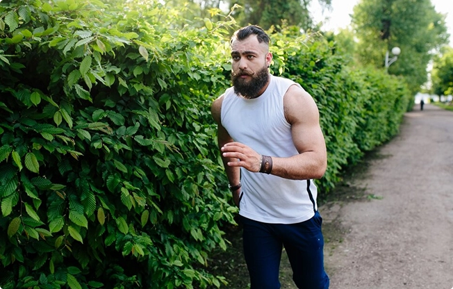 A bearded man running along a scenic path surrounded by greenery A bearded man running along a scenic path surrounded by greenery