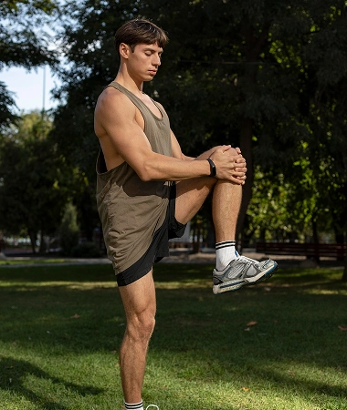A man in a tank top stretches his arms in a sunny park, surrounded by green grass and trees A man in a tank top stretches his arms in a sunny park, surrounded by green grass and trees.