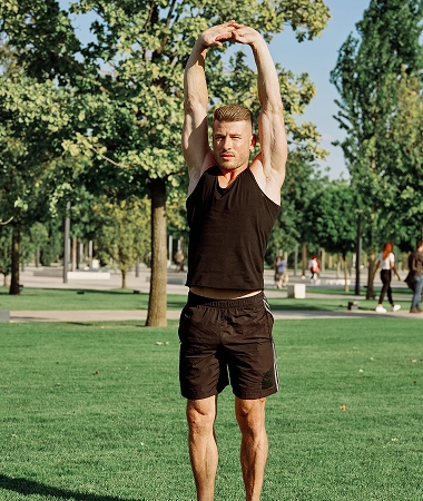 A man performs a handstand on grass in a park, surrounded by trees and a clear blue sky A man performs a handstand on grass in a park, surrounded by trees and a clear blue sky.
