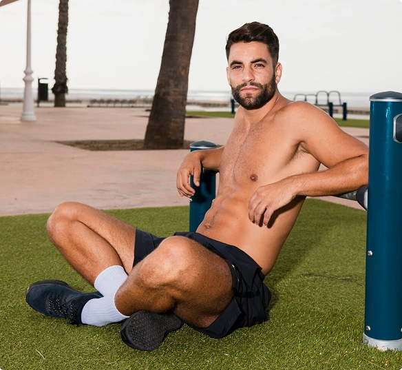 A shirtless man sits on a bench by the beach, gazing at the ocean waves under a clear blue sky A shirtless man sits on a bench by the beach, gazing at the ocean waves under a clear blue sky.