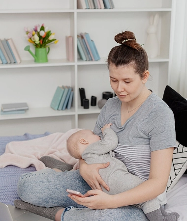 A woman sits on a bed, gently holding a baby in her arms, both looking content and relaxed A woman sits on a bed, gently holding a baby in her arms, both looking content and relaxed