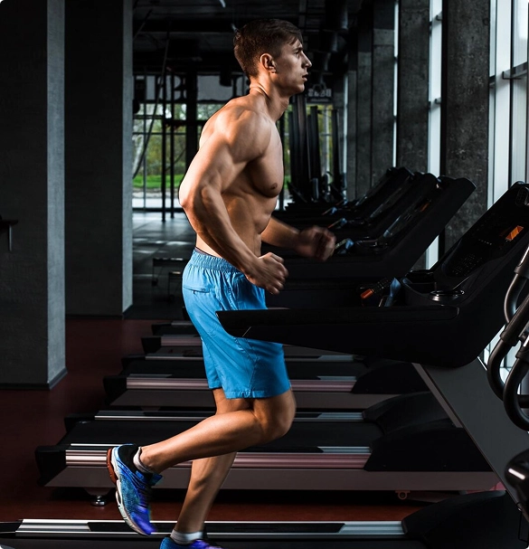 A shirtless man running on a treadmill in a gym, focused on his workout amidst various gym equipment.