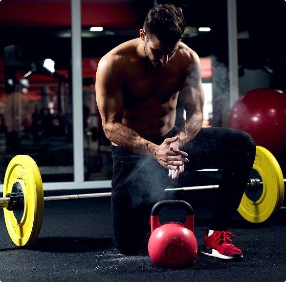A man is in a squat position, facing a red kettlebell, indicating readiness for strength training.