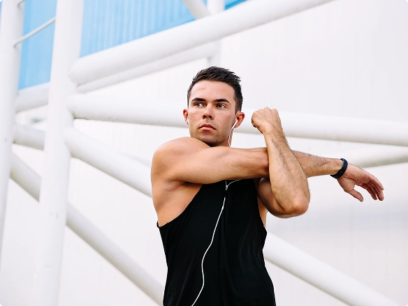 A man wearing a black tank top extends his arm to the side, demonstrating a stretching exercise. A man wearing a black tank top extends his arm to the side, demonstrating a stretching exercise.