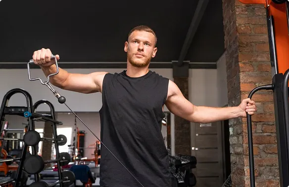In a gym setting, a man holds a rope, likely for strength training or functional fitness exercises.