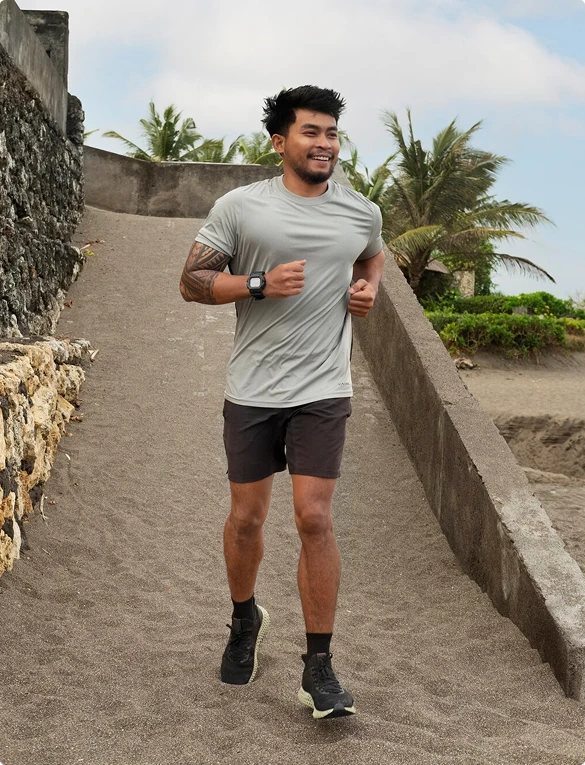 A man in a grey shirt and shorts runs along a path surrounded by greenery.