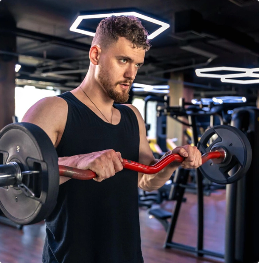 A man weight training with an EZ curl barbell in the gym to build strength and stamina.
