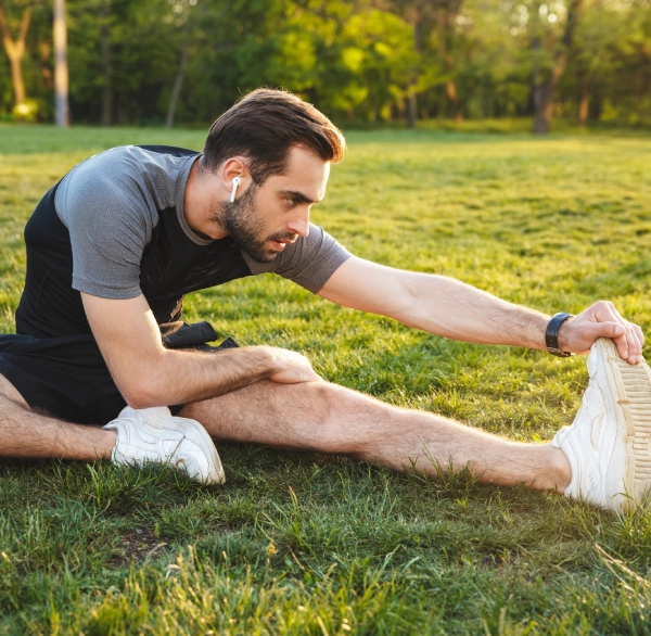 A man stretches his legs while sitting on green grass in a sunny outdoor setting.