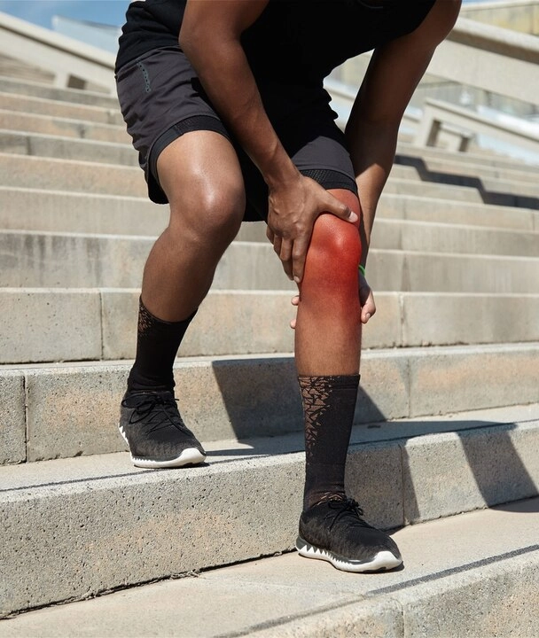 A man with a knee injury struggles to navigate stairs, using a handrail for support.